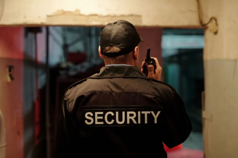 Agent de sécurité de dos, veste marquée Security, dans un couloir