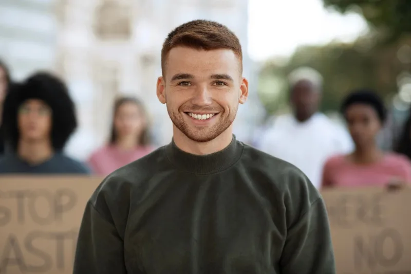Homme souriant en pull sombre, photographié en extérieur